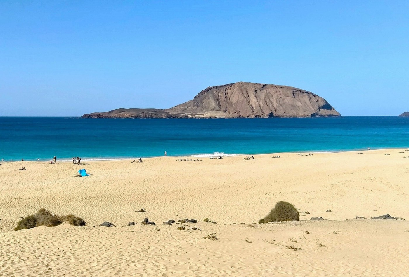 Playa de las Conchas con arena dorada, mar azul y el islote de Montaña Clara enfrente