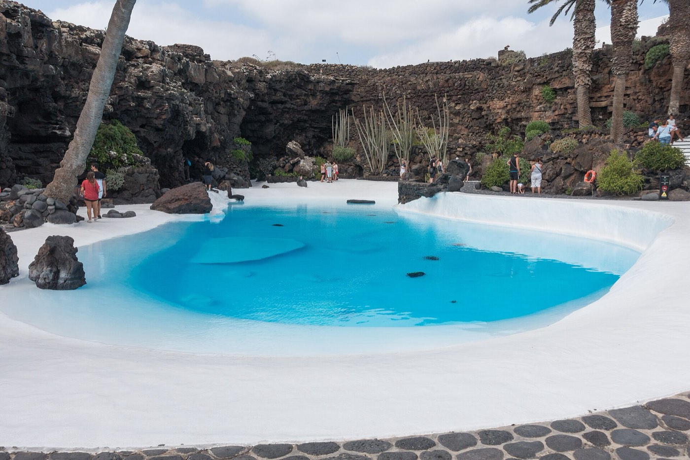 Piscina blanca y turquesa de los Jameos del Agua rodeada de roca volcánica y palmeras